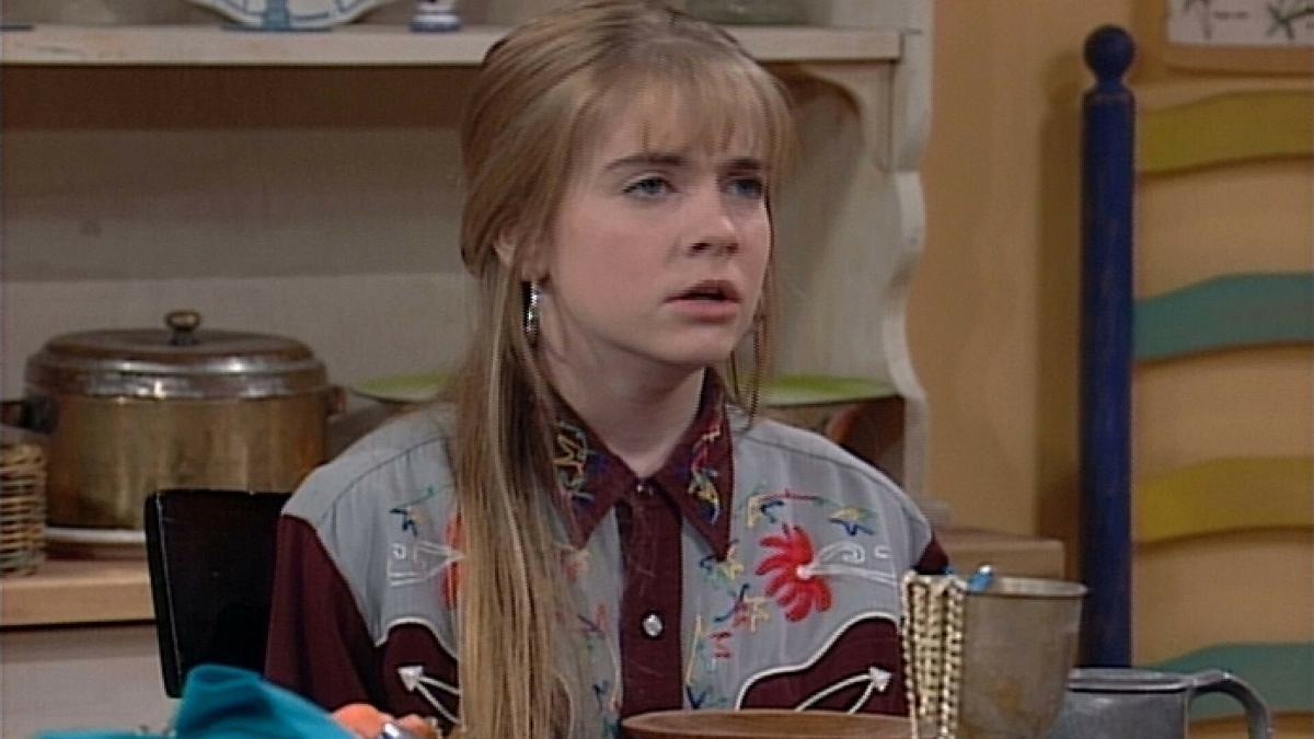 Still from the 90's show 'Clarissa Explains it All', it depicts the title character sitting at her kitchen table wearing an embroidered denim button up shirt with black details.